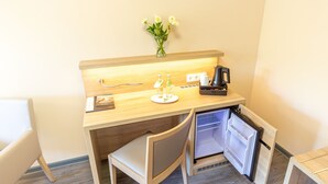 Una kitchenette compacta con cafetera, un refrigerador pequeño y un florero con flores en la encimera.
