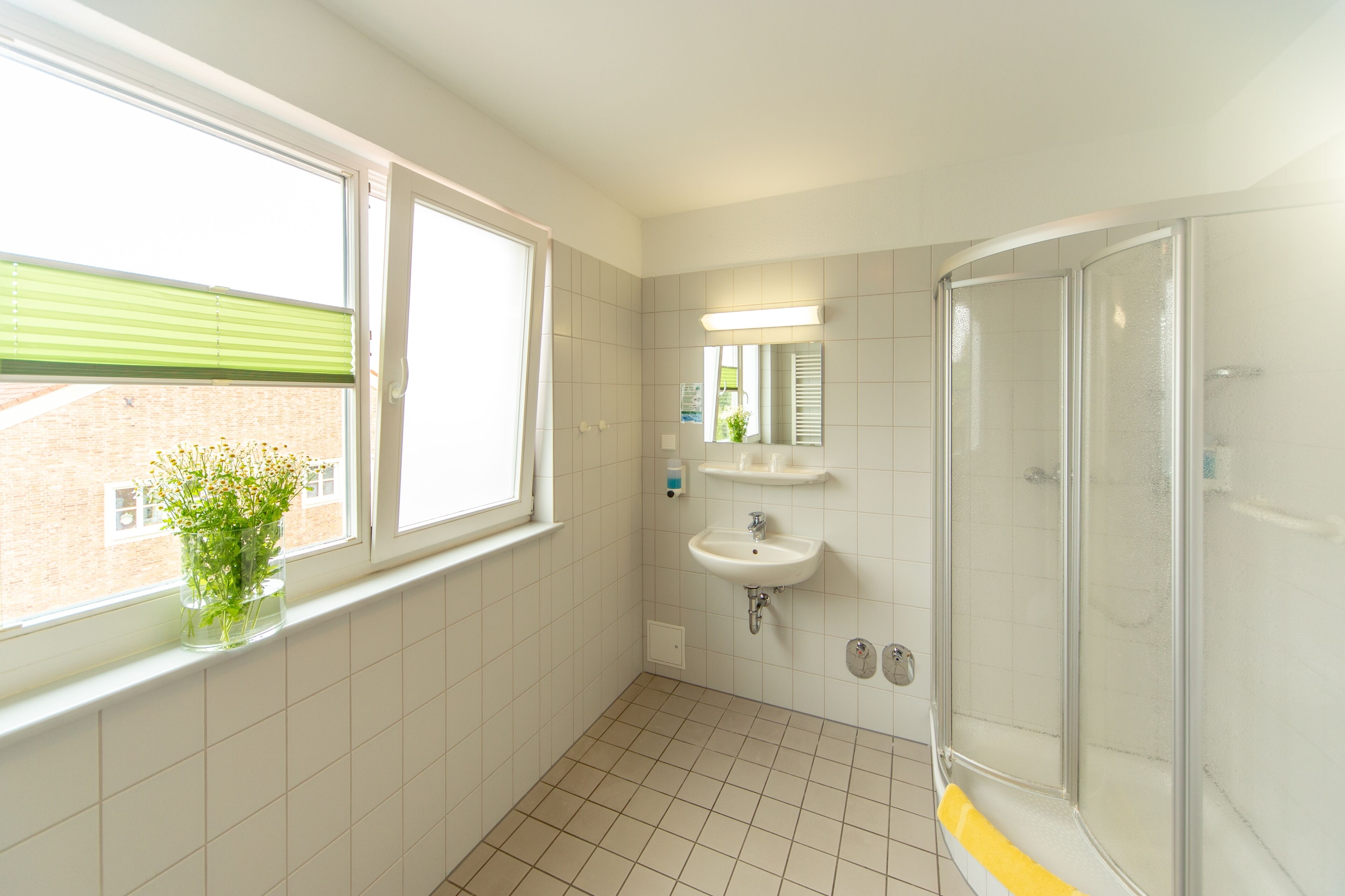 Ein Badezimmer mit Fenster, Waschbecken, Spiegel und Dusche.