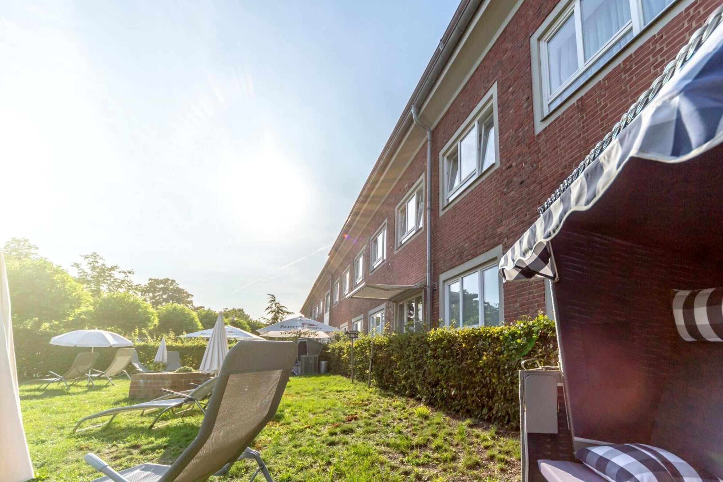 A brick building with a well-maintained lawn, outdoor seating area with chairs and umbrellas, and a clear sky.