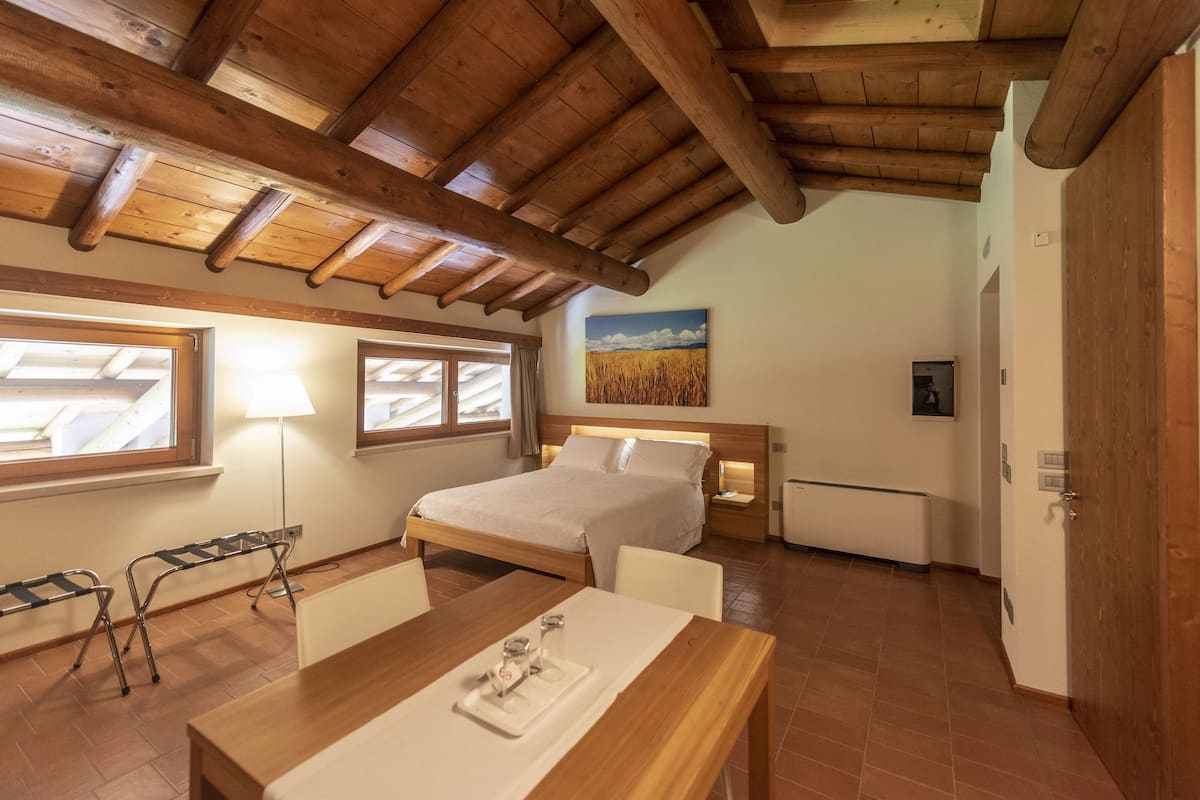 A bedroom with a wooden ceiling, a bed, bedside tables, a desk with a tray, and a window with curtains.