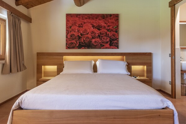 Una cama bien hecha con un cabecero de madera, una obra de arte en la pared con rosas rojas y una mesita de noche con una lámpara.