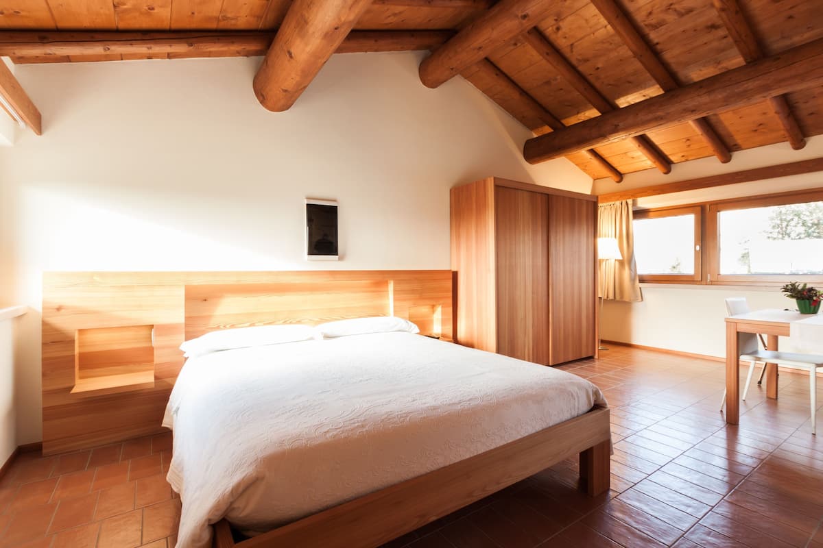 A bedroom with a wooden bed, a wardrobe, a desk, and a window.