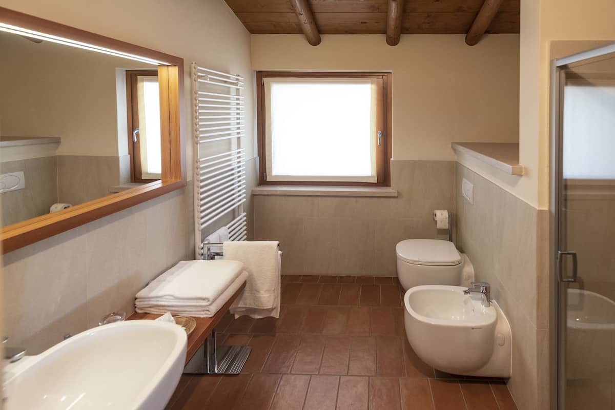 A bathroom with a bathtub, bidet, toilet, and a window with blinds.