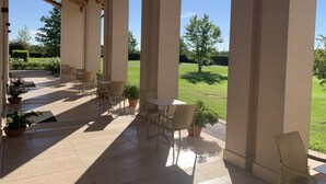 Un patio couvert avec un sol carrelé, plusieurs tables et chaises, et des plantes en pot.