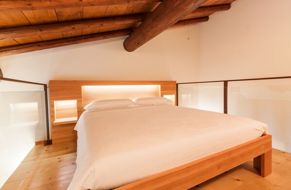 A bedroom with a wooden bed frame, a sloped ceiling, and a glass partition.