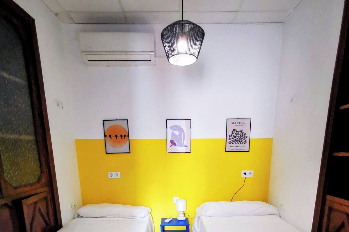 A hotel room with two beds, a small table with a lamp, and artwork on the wall.