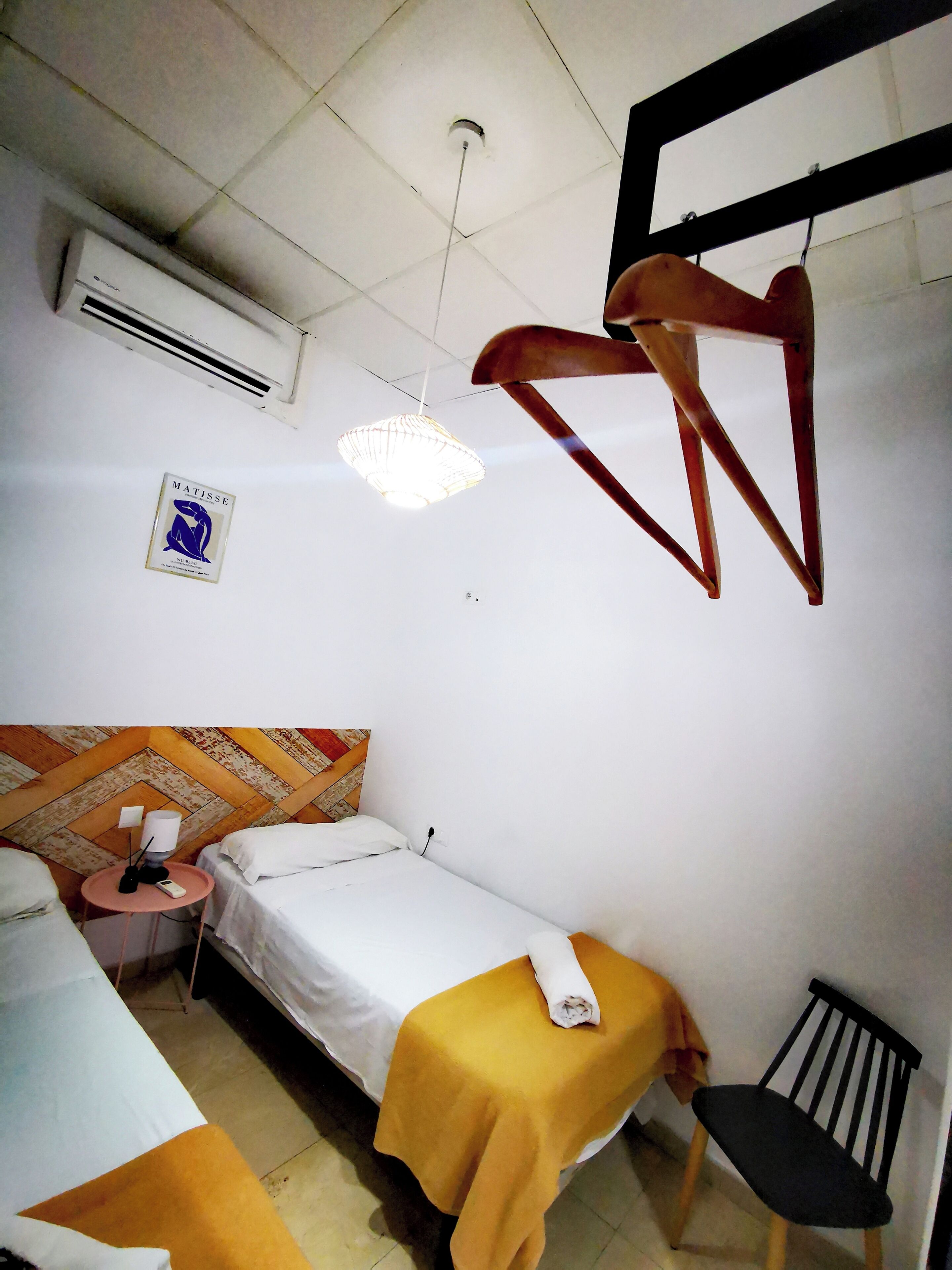 Una habitación pequeña y sencilla con cama, una silla, una mesa y una lámpara colgante.
