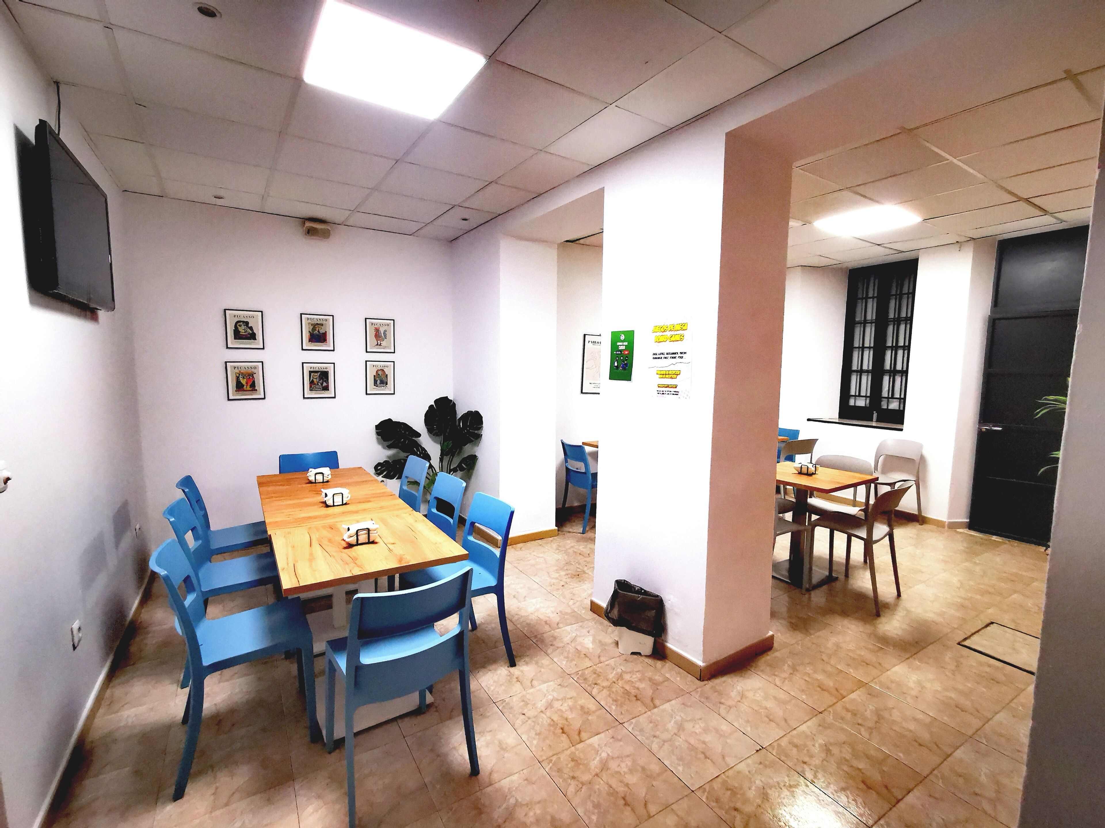 A conference room with a long table, blue chairs, a wooden table, and a TV on the wall.