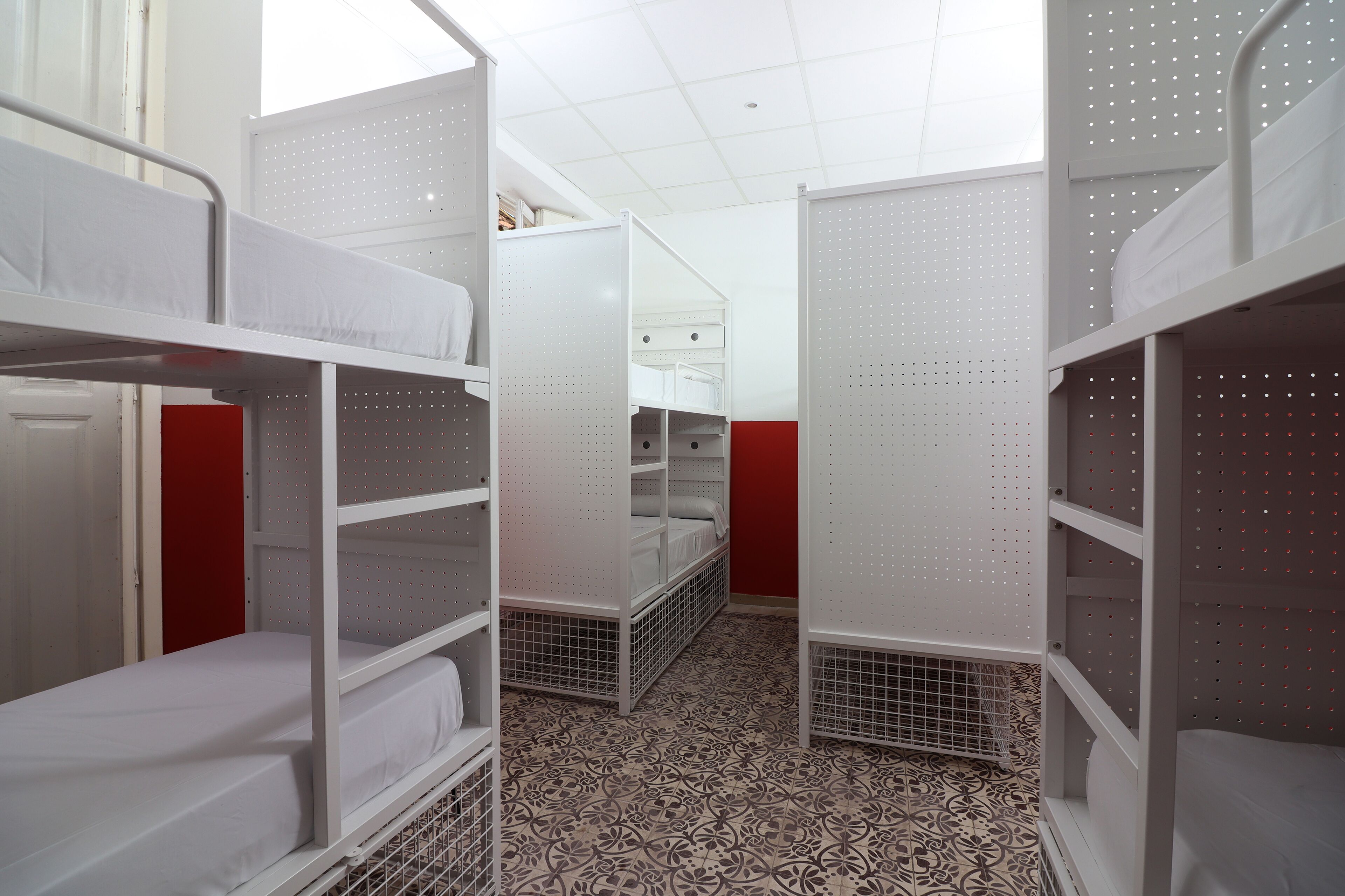 A dormitory room with bunk beds, a tiled floor, and a red accent wall.