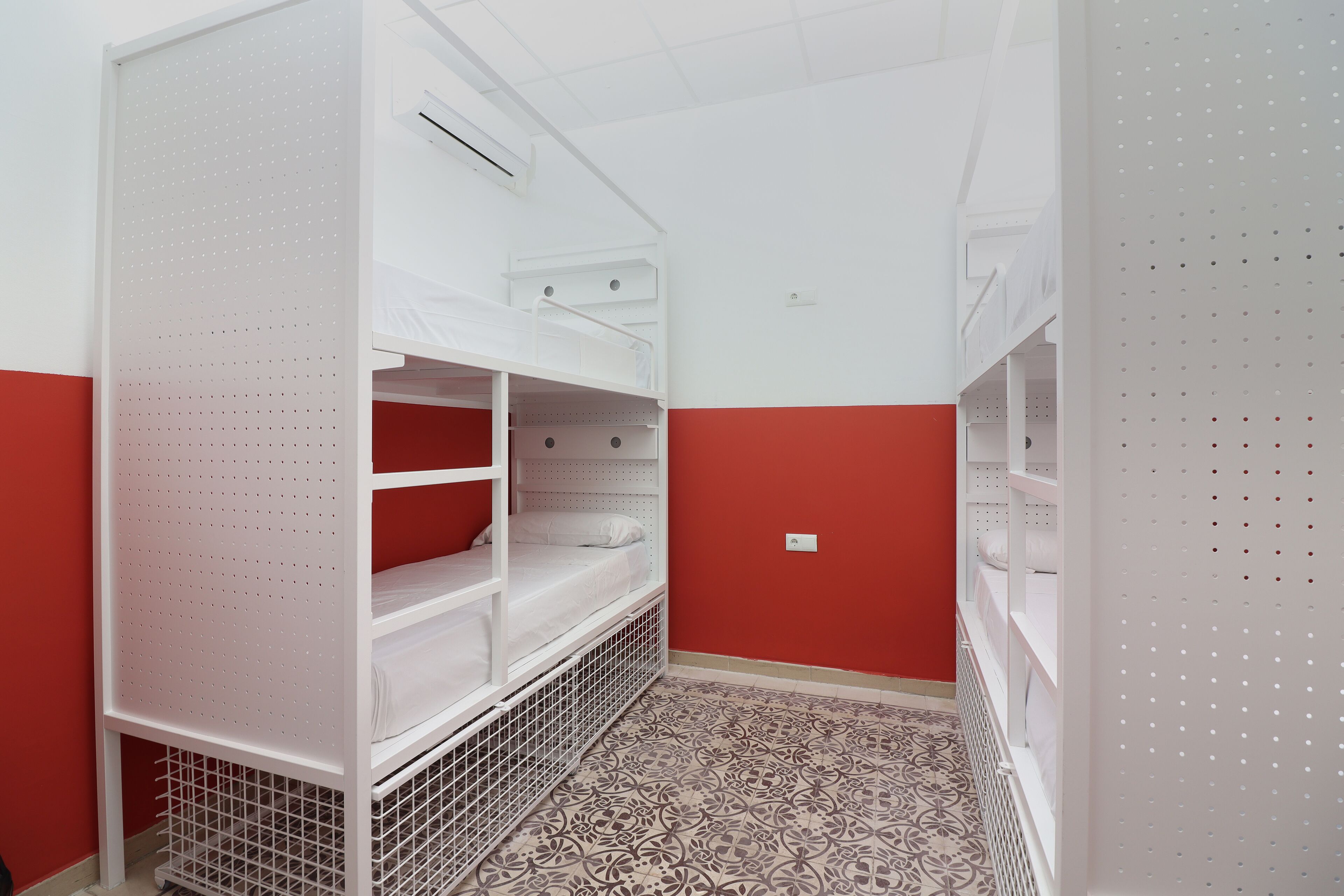 Une chambre avec des lits superposés, un mur rouge et un revêtement de sol à motifs.