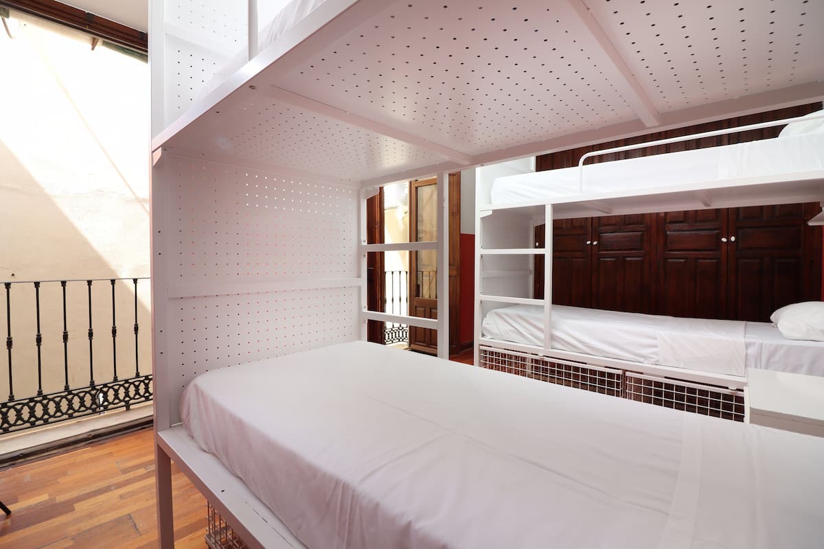 A bunk bed room with a wooden floor, white bedding, and a balcony with a metal railing.