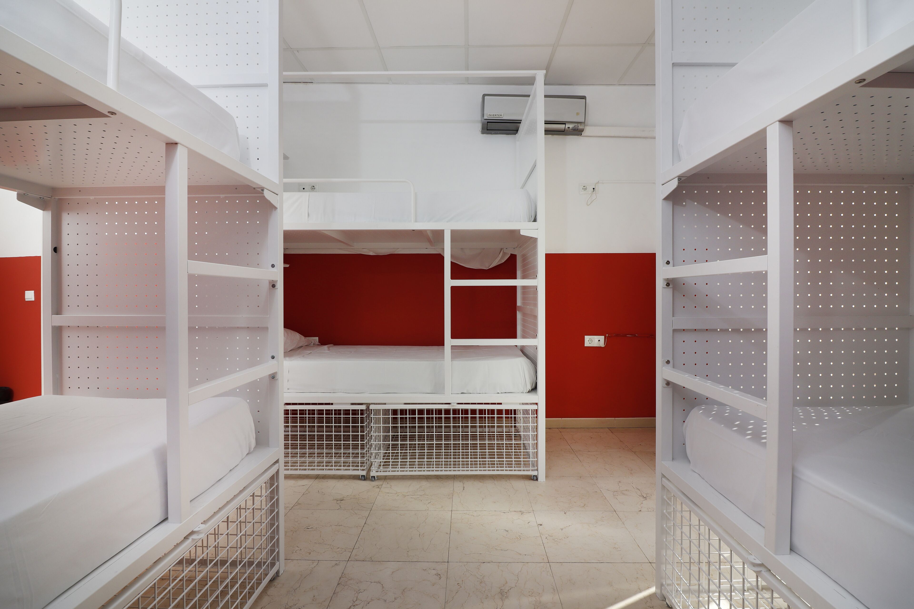 A bunk bed room with a red wall, white metal shelving, and a tiled floor.