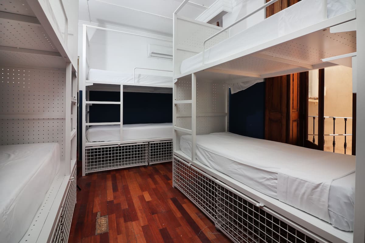 A compact, multi-level bunk bed room with white bedding and a wooden floor.