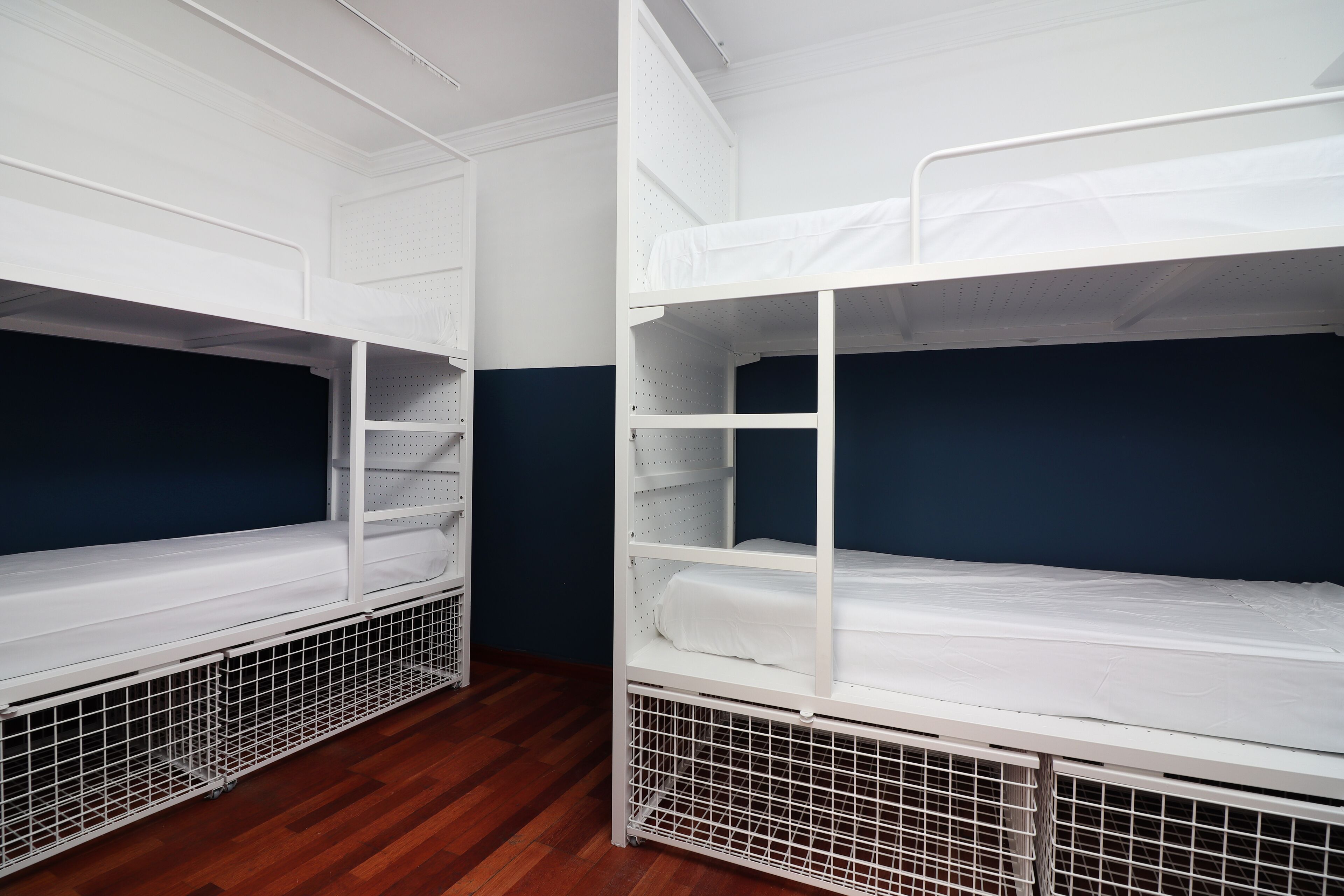 Deux lits superposés avec des structures en métal, du linge de lit blanc et un mur bleu foncé.