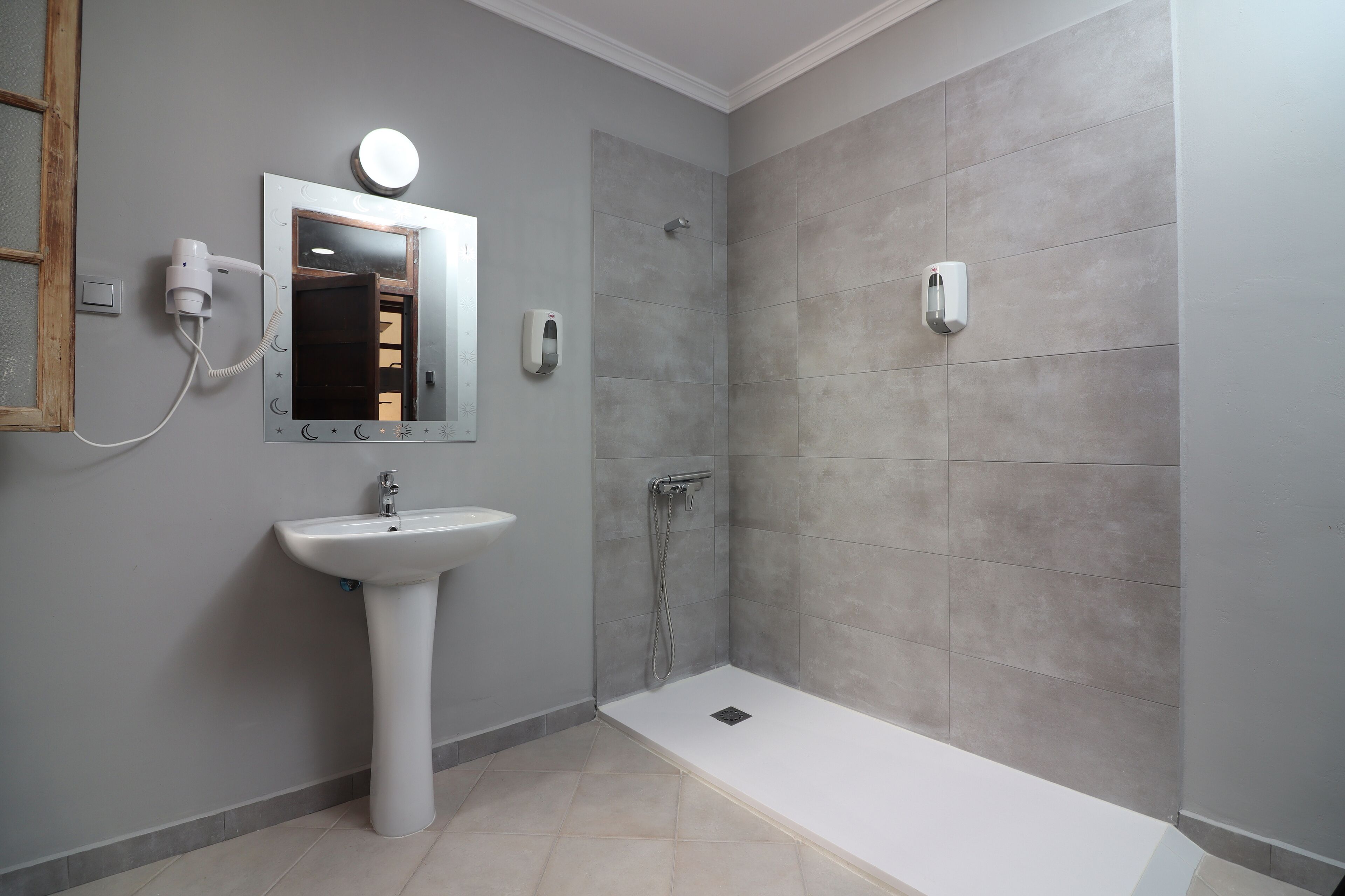 Ein Badezimmer mit einem Waschbecken auf Säule, einem Spiegel, einem Handtrockner und einer Handbrause sowie einer eingebauten Toilette.