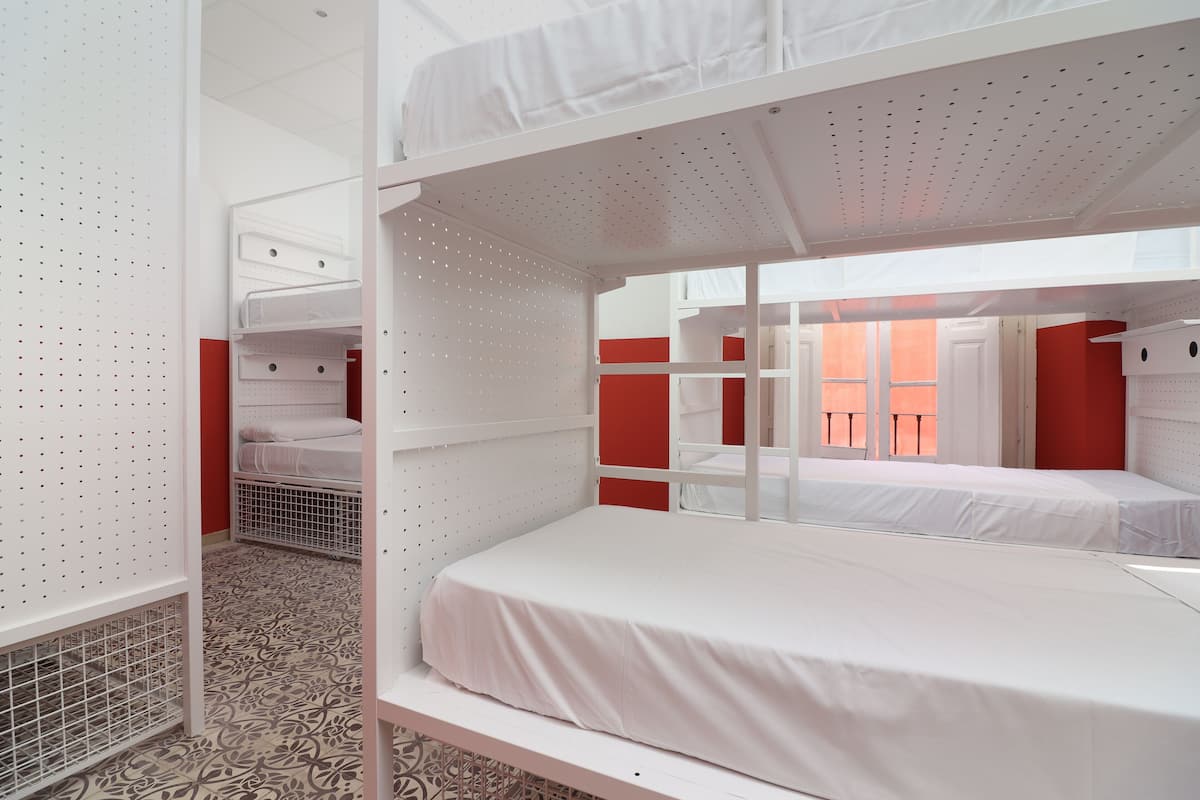 A dormitory room with bunk beds, a patterned floor, and a red accent wall.