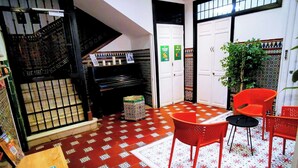 Una habitación con piso estampado, una escalera, una mesa con folletos y una puerta con un cartel.
