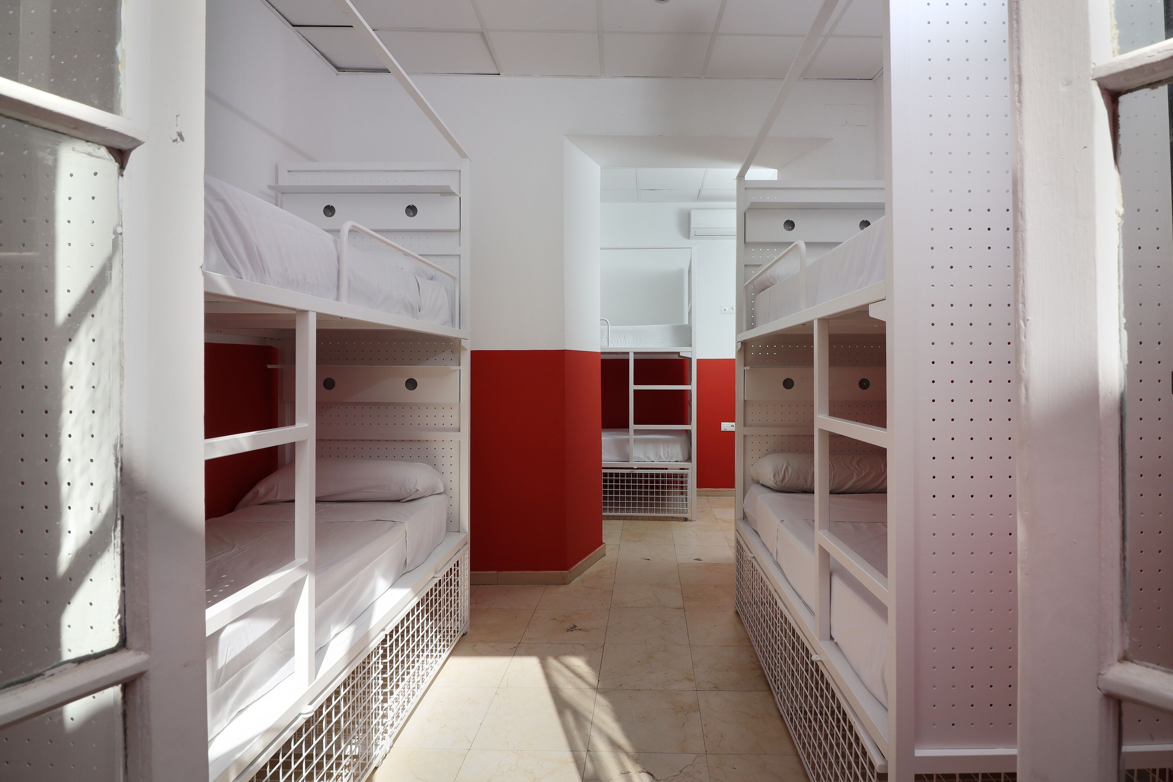 A dormitory with bunk beds, a red accent wall, and a tiled floor.