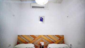 Een kleine hotelkamer met twee bedden, een bureau, een stoel, een bekeken hoofdbord, een airconditioning en een plafondlamp.