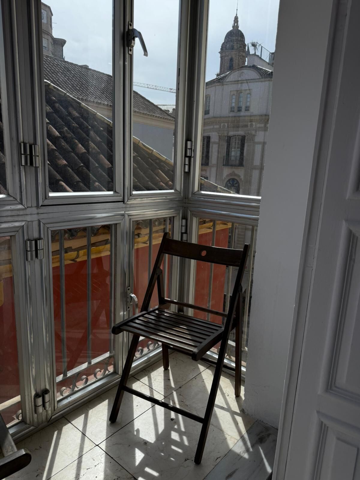 A room with large windows, a metal chair, and a view of buildings.