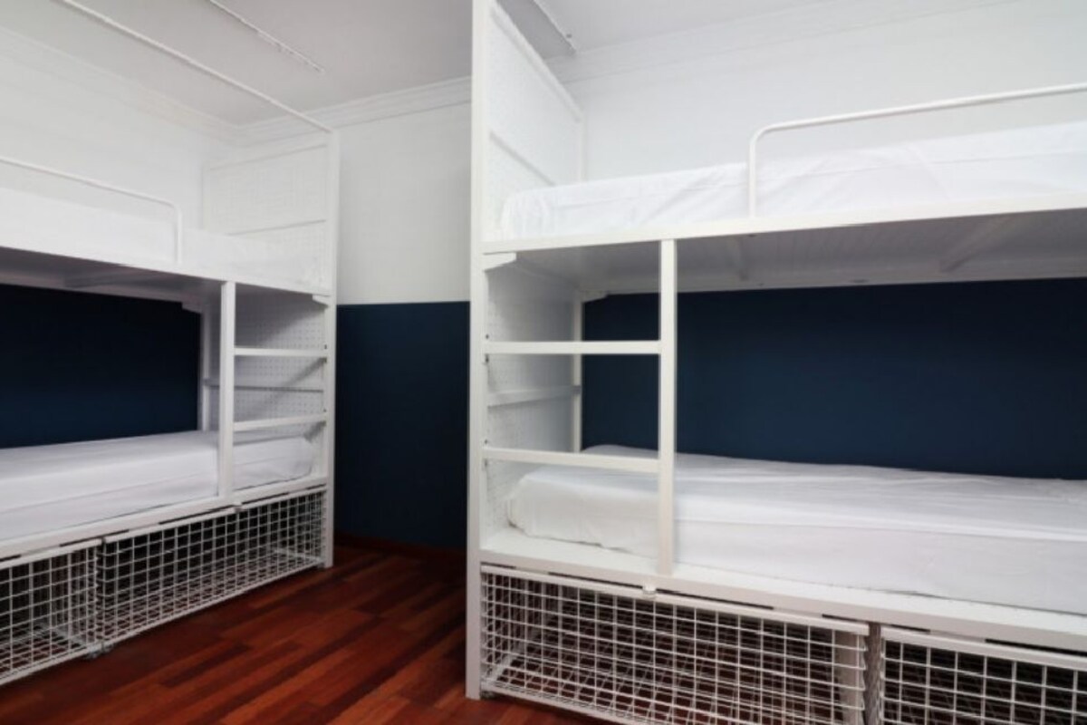 Two bunk beds with white frames and blue mattresses, in a room with wooden flooring and dark blue walls.