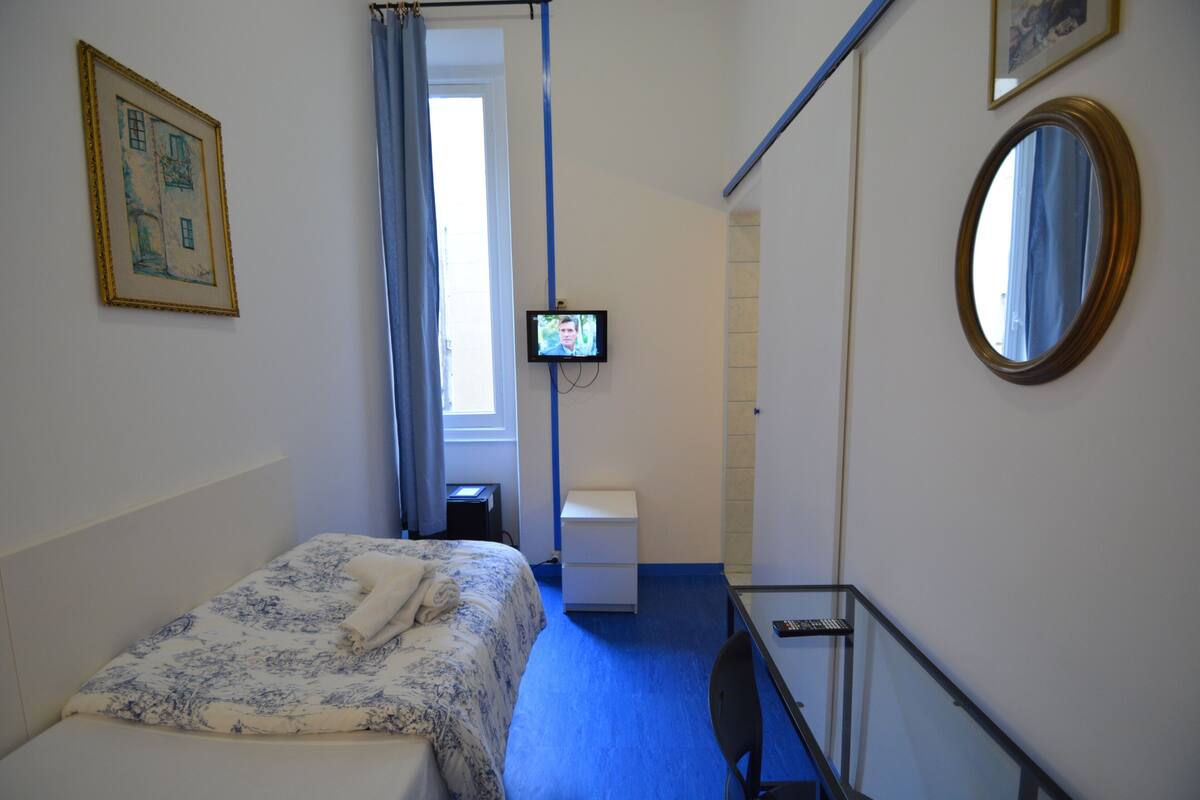 A hotel room with a bed, a desk, a chair, a television, a mirror, and a window with curtains.