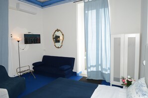 A hotel room with a bed, a sofa, a mirror, a TV, and a wardrobe. - Olympia Hotel (Genoa)