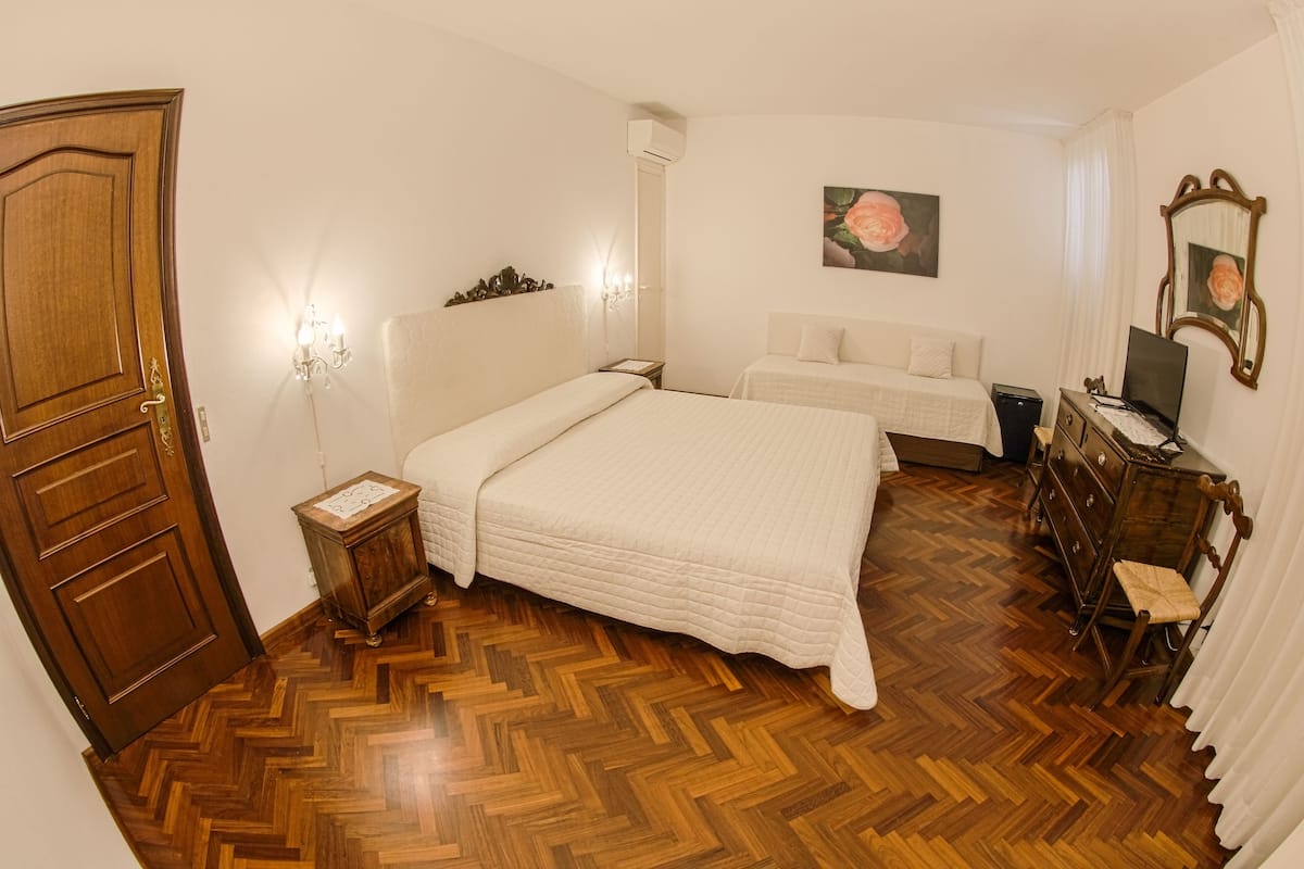 A bedroom with two beds, a wooden floor, a dresser, a mirror, and a painting on the wall.
