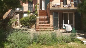 Un edificio de dos pisos con una escalera que lleva a la entrada, rodeado de follaje.