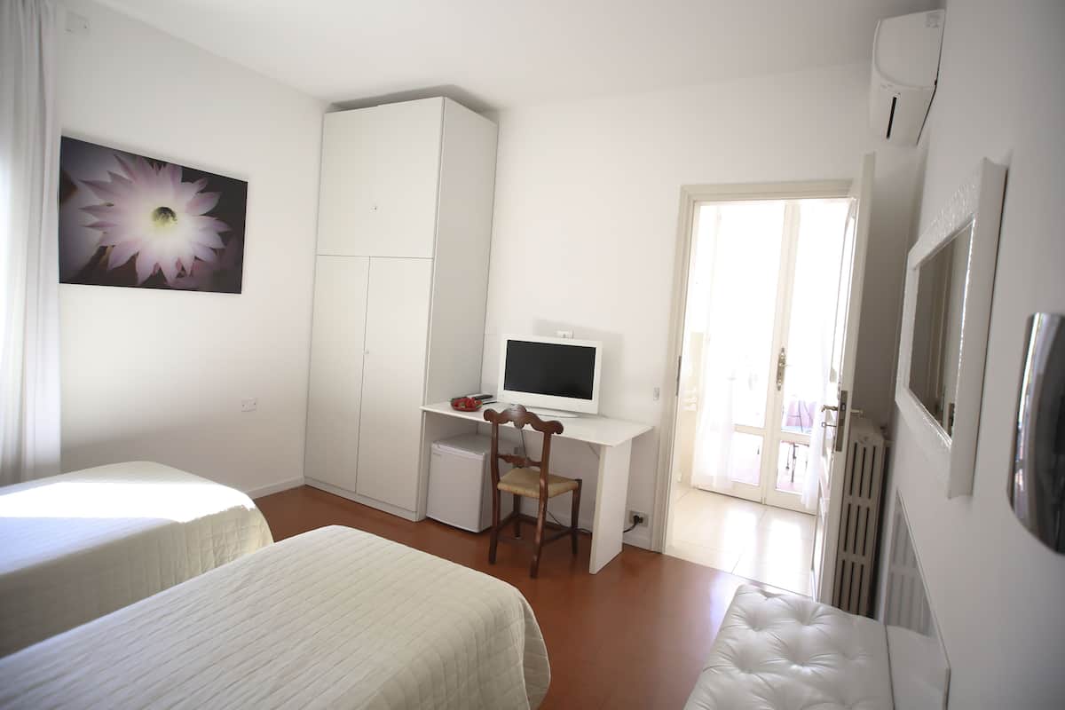 A bedroom with two beds, a desk with a computer, a chair, and a radiator.