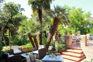 An outdoor patio with wicker furniture, a table set for dining, and a variety of potted plants. - Ai Giardini di San Vitale (Ravenna)