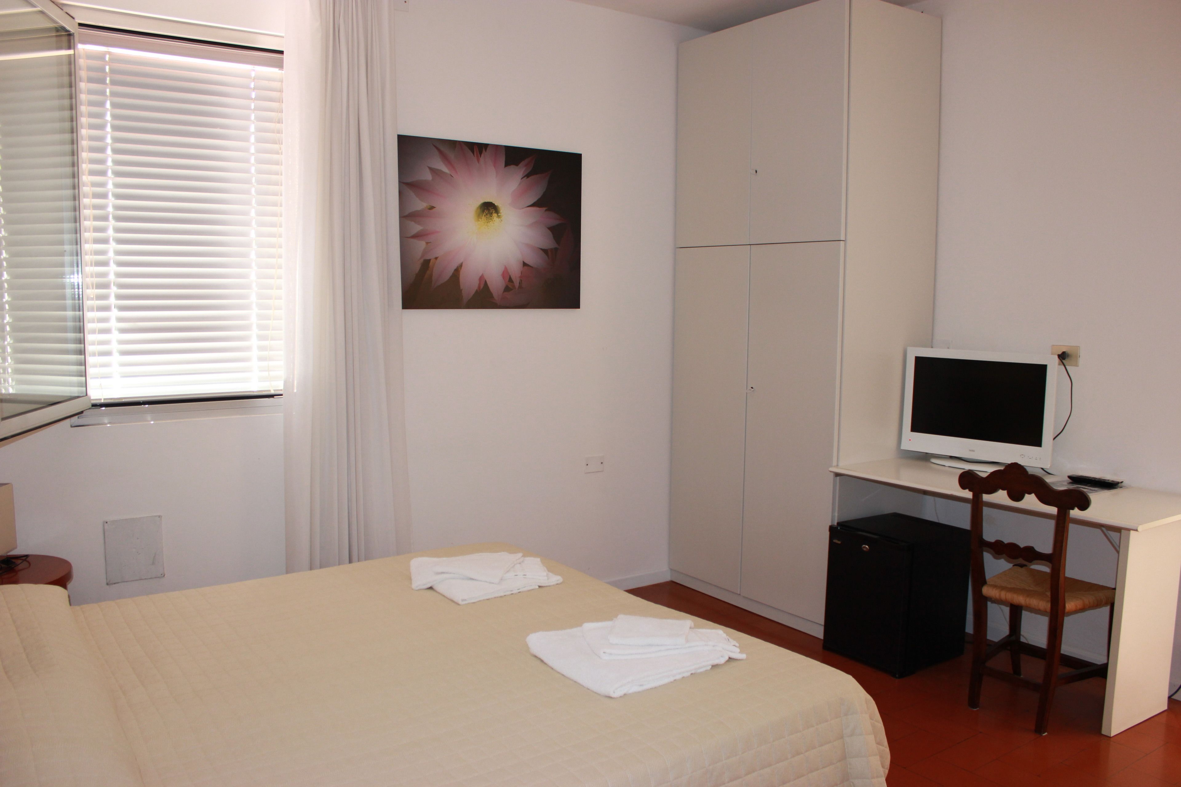 A hotel room with a bed, a desk with a computer, a chair, and a window with blinds.