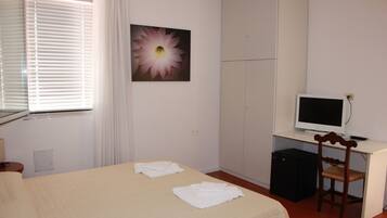 A hotel room with a bed, a desk with a computer, a chair, and a window with blinds.