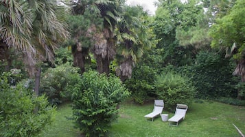 A lush garden with two white lounge chairs and a small table.