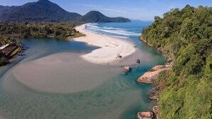 Paesaggio costiero con spiaggia sabbiosa, acque cristalline e vegetazione lussureggiante.
