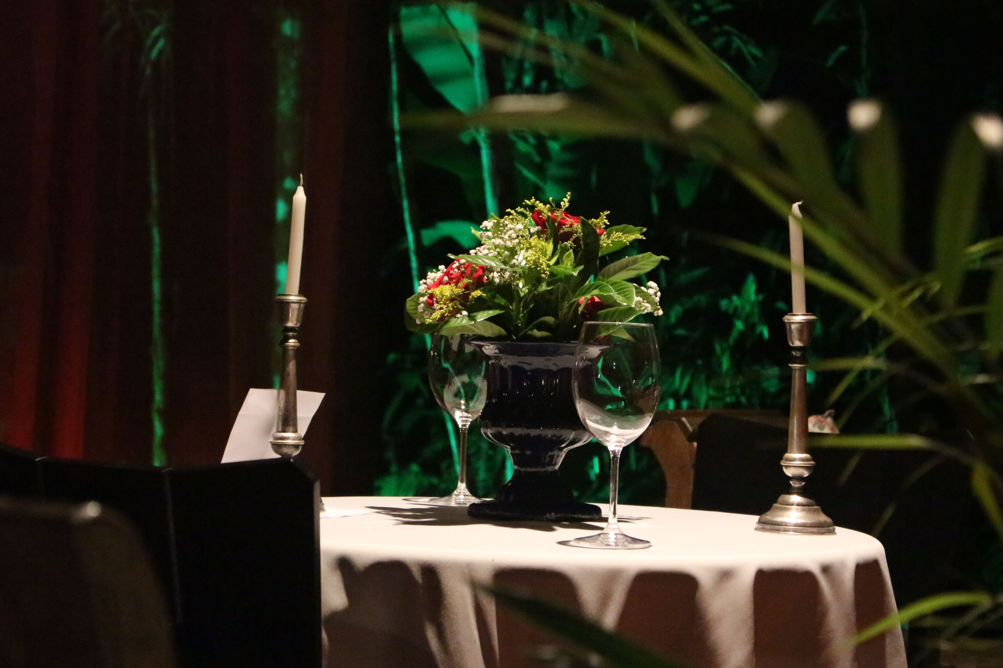 Uma mesa posta com um vaso de flores, duas taças de vinho e duas velas.