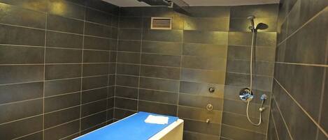 A bathroom with dark tiled walls, a blue countertop, and a shower with a handheld showerhead.