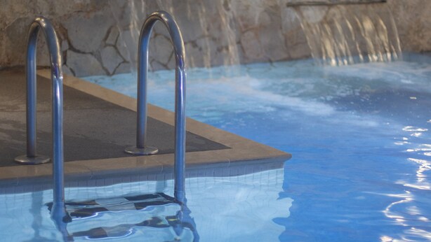 Una piscina con escaleras metálicas, un muro de piedra y una fuente de agua.