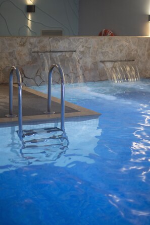 A swimming pool with metal ladders, a stone wall, and a water feature. - Hotel & Spa La Terrassa (Castell-Platja d'Aro)