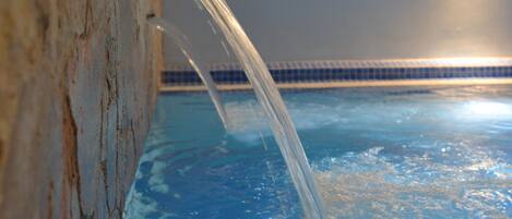 Una piscina con agua que fluye desde una pared, un borde de azulejos y un accesorio de luz empotrado.