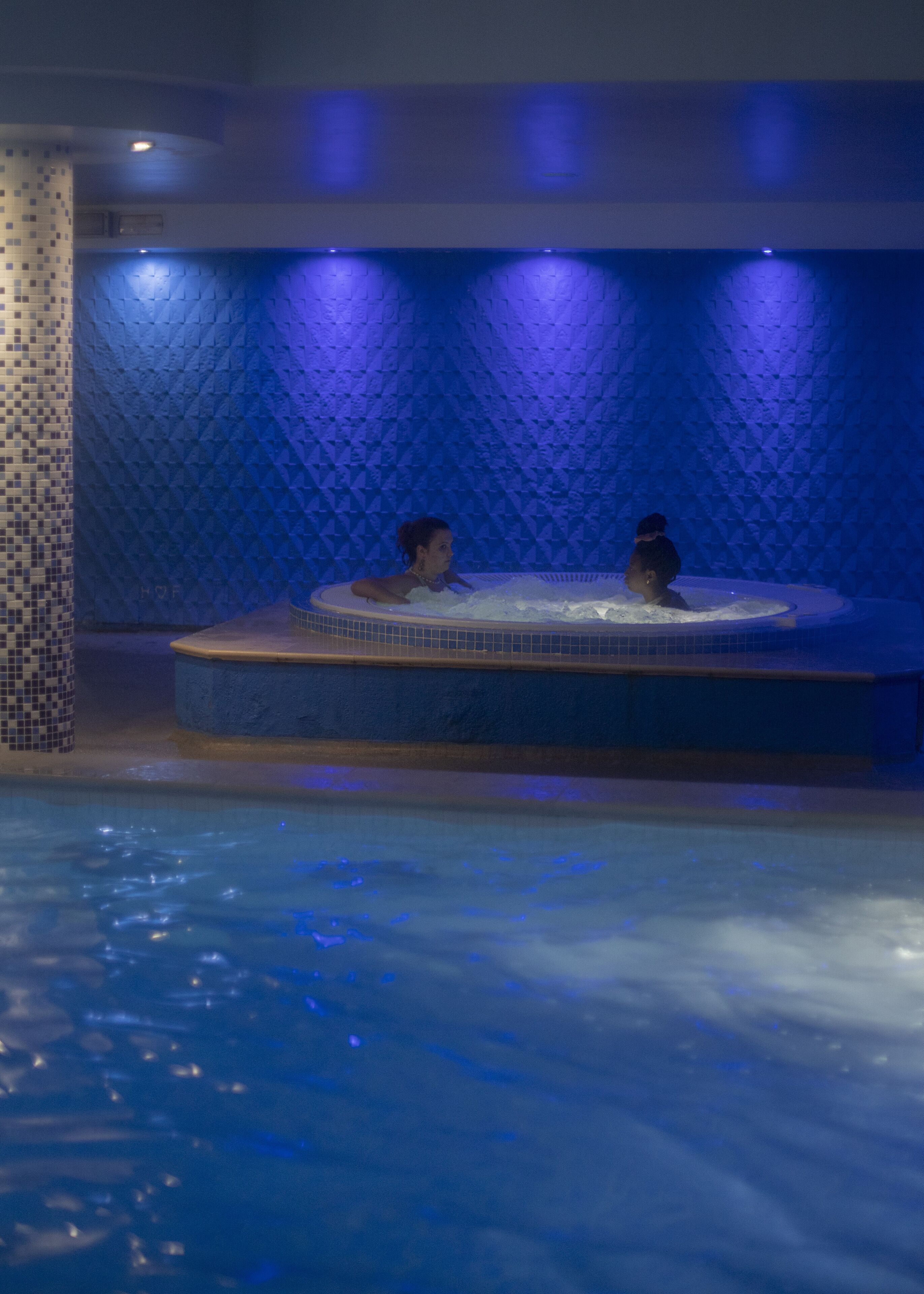A hot tub with two people in a dimly lit room with blue lighting.