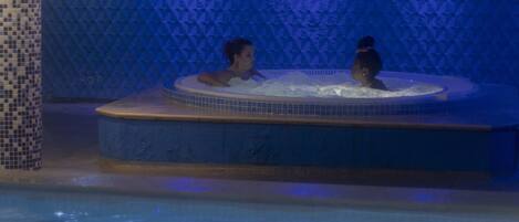A hot tub with two people in a dimly lit room with blue lighting.