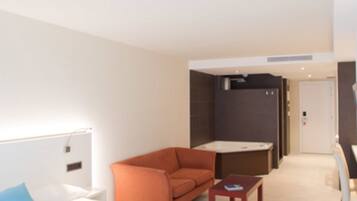 Habitación de hotel moderna con cama, sofá, una mesita y baño visible a través de una puerta.