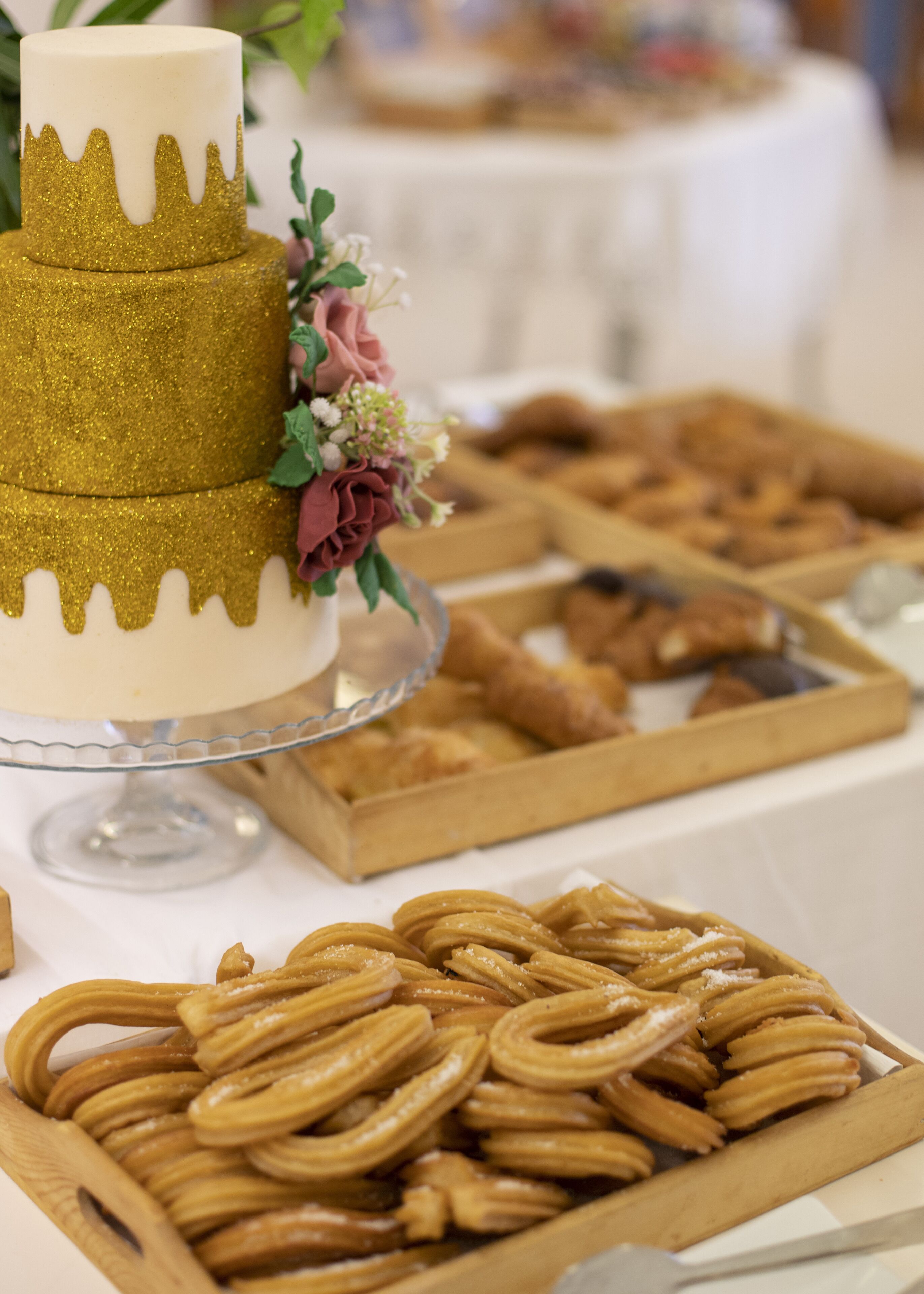 Un gâteau à étages, avec une base dorée et scintillante et un sommet blanc, entouré de diverses pâtisseries et de desserts disposés sur une table.