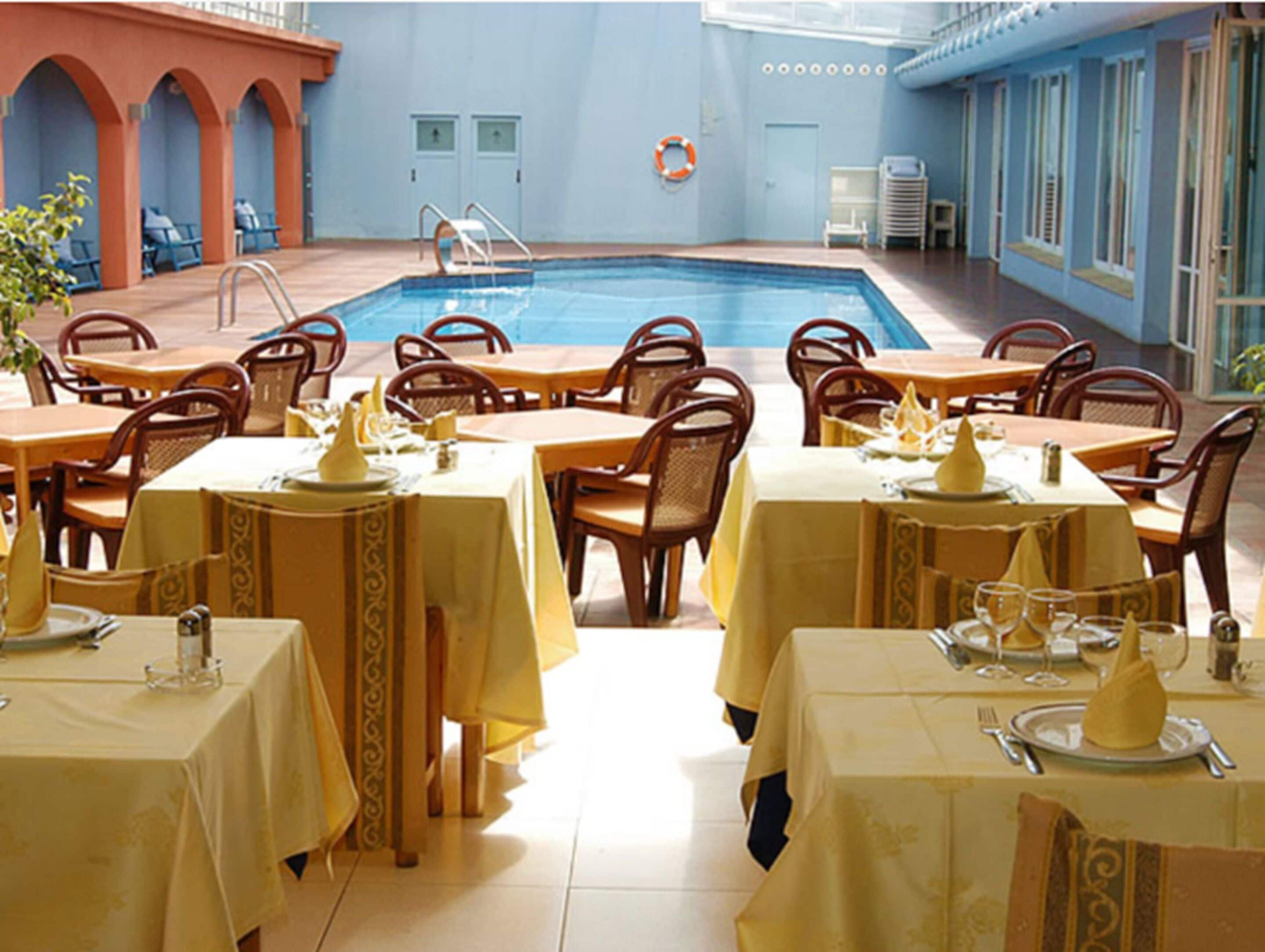 Un restaurante junto a la piscina con mesas dispuestas para comer, una piscina y un flotador en la pared.