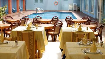 Un restaurante junto a la piscina con mesas dispuestas para comer, una piscina y un flotador en la pared.
