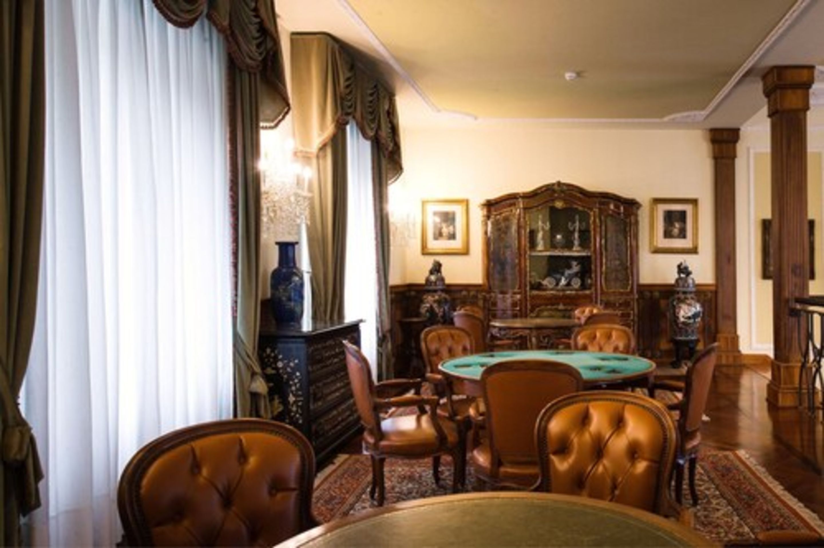 A formal dining room with a green poker table, leather chairs, and a classic wooden cabinet with glass doors.