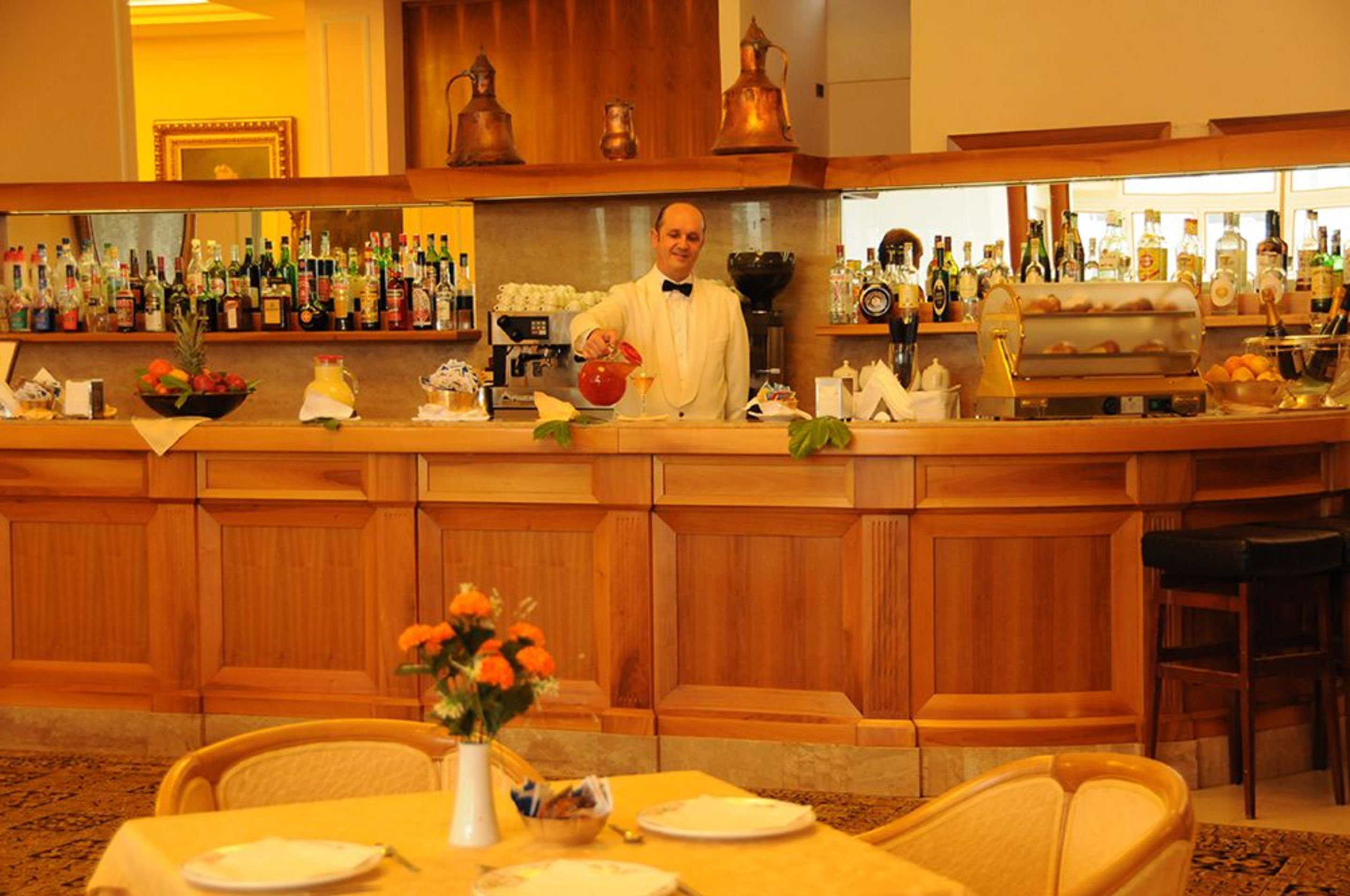 Zona de bar con un cantinero, una variedad de botellas y una mesa de buffet.