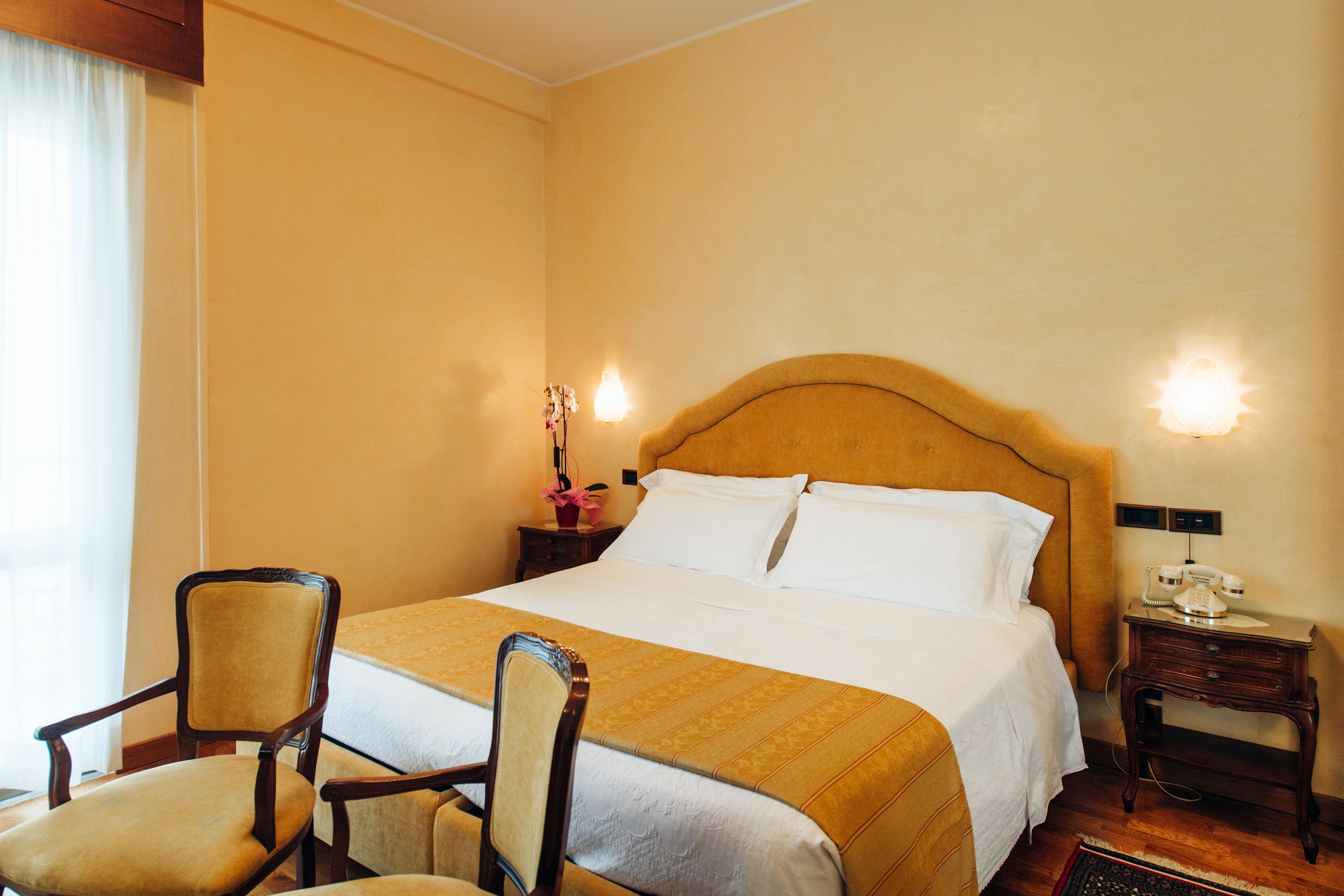 A hotel room with a large bed, two bedside tables, a chair, and a nightstand with a telephone.