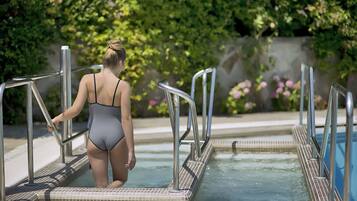 A person in a swimsuit standing at the edge of a pool with metal railings.